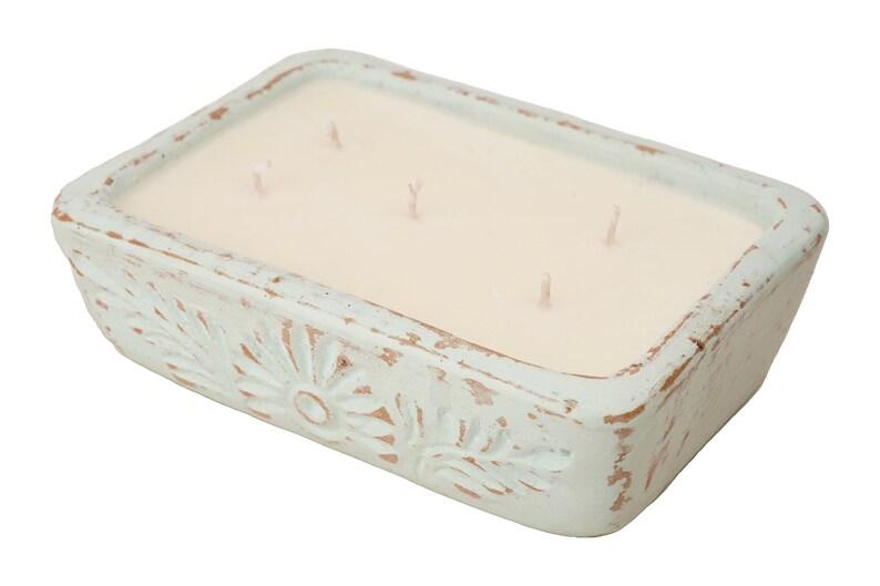 Pu&ograve; includere: Un portacandele rettangolare in ceramica blu chiaro con una candela bianca all'interno. Il portacandele ha una finitura usurata e un motivo floreale.