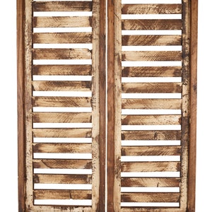 May include: Two wooden shutters with a distressed white paint finish. The shutters are made of horizontal slats and have a dark brown frame.