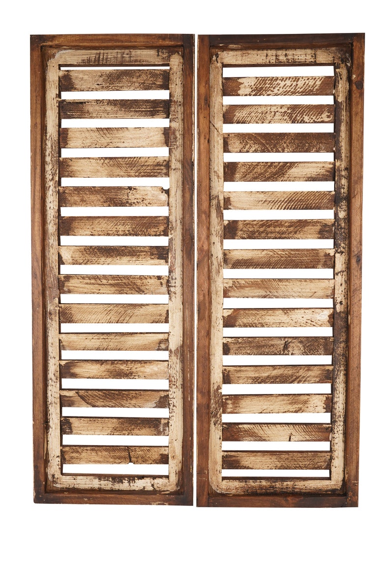 May include: Two wooden shutters with a distressed white paint finish. The shutters are made of horizontal slats and have a dark brown frame.