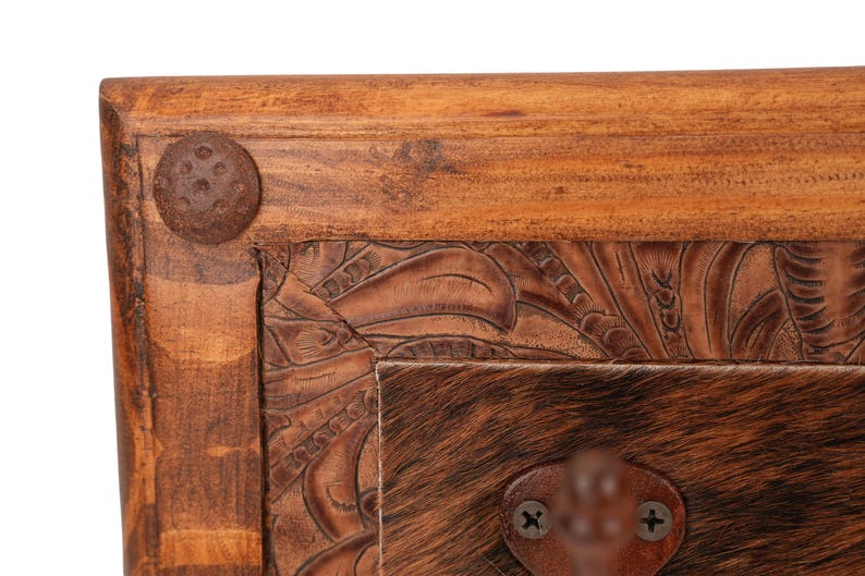 May include: Close-up of a wooden furniture corner. The frame is made of light brown wood with a dark brown, textured metal rivet. The center features a brown leather panel with carved floral designs and a section of brown and tan animal hide.