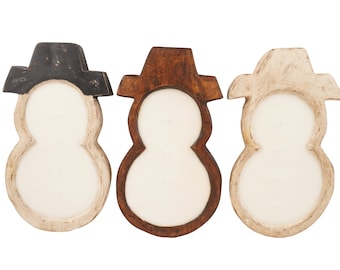 May include: Three wooden snowman candle holders with different colored hats. The snowman on the left has a black hat, the middle snowman has a brown hat, and the snowman on the right has a white hat.