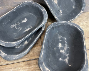 May include: Four black wooden dough bowls with a distressed white paint finish. The bowls are oval shaped and have a rustic look.