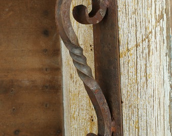 May include: A rusty metal door handle with a twisted design, mounted on a weathered wooden door.