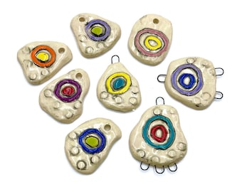 May include: Eight ceramic pendants with colorful concentric circles painted on a white background. Each pendant has a hole at the top for hanging.