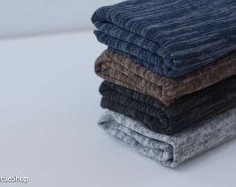 May include: A stack of folded fabric in shades of blue, brown, black, and gray. The fabric has a textured, heathered appearance. The layers are neatly stacked on a white surface, showcasing the different color options available.