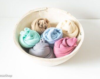 May include: A rustic, off-white bowl filled with six rolled-up fabric items in various pastel colors: beige, mint green, light blue, lavender, pale yellow, and pink. The bowl has a natural, weathered appearance.