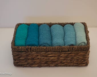 May include: A wicker basket filled with six rolled up fabric swatches in shades of blue and teal.