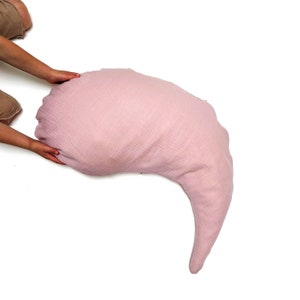 May include: A large, crescent-shaped pink pillow made of soft, textured fabric. The pillow is ideal for cuddling and providing support.