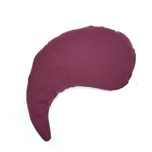 Puede incluir: Una almohada de lactancia de color burdeos en forma de media luna. La almohada está hecha de un tejido suave y texturizado.