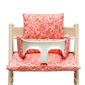 May include: A pink and white floral high chair cushion with a white tray. The cushion has a floral pattern with pink, white, and brown flowers.