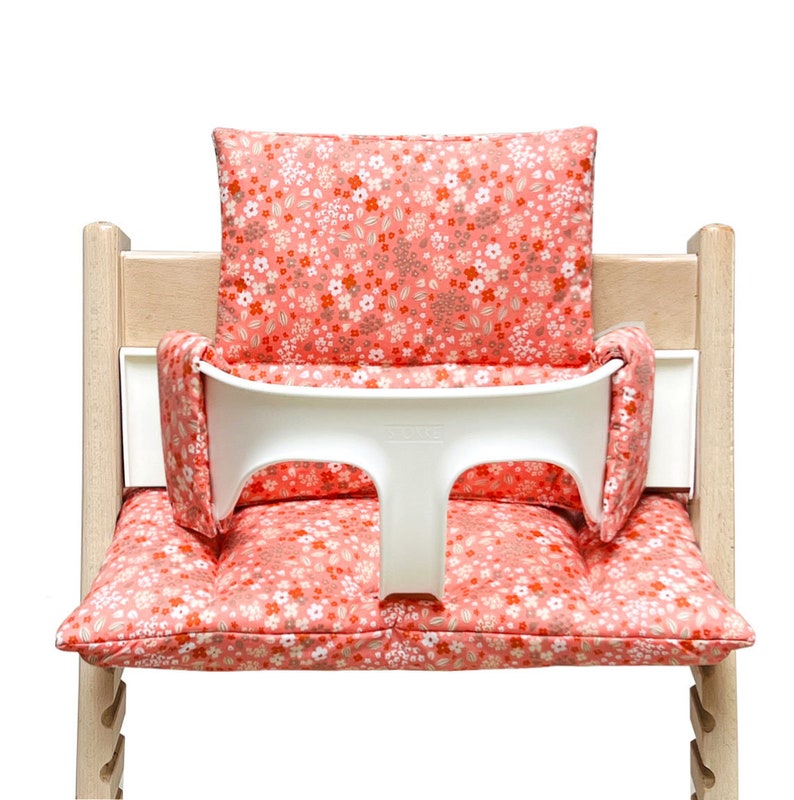 May include: A pink and white floral high chair cushion with a white tray. The cushion has a floral pattern with pink, white, and brown flowers.