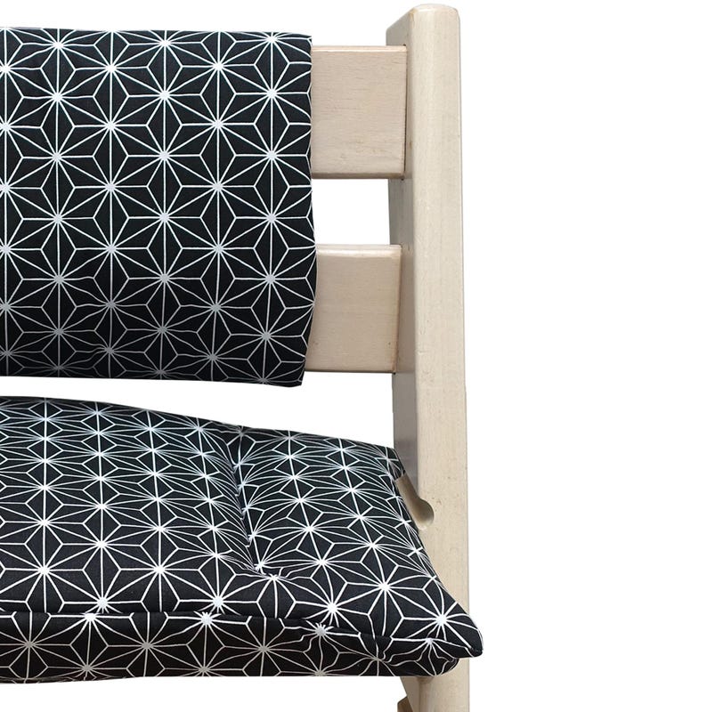 K&ouml;nnte beinhalten: Ein h&ouml;lzerner Hochstuhl mit einem schwarz-wei&szlig;en geometrischen Kissen und einer R&uuml;ckenlehne. Das Muster ist ein sich wiederholendes Design aus wei&szlig;en sternartigen Formen auf schwarzem Hintergrund. Der Stuhlrahmen ist hell und hat eine nat&uuml;rliche Holzfarbe.