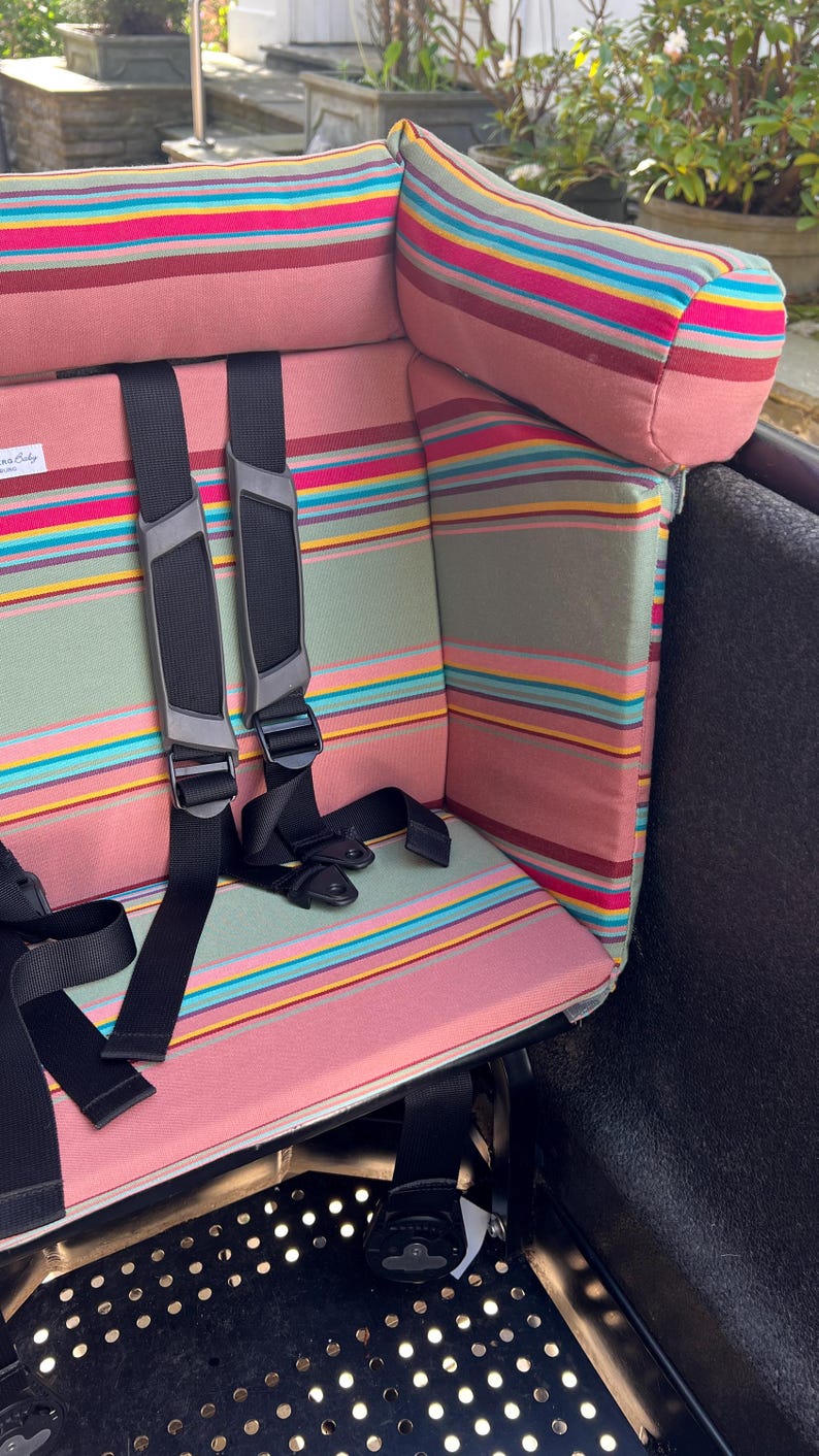 Ein rosa-grün gestreiftes Kissen für das Lovens Lastenrad. Das Polster für das Cargobike passt auch für Urban Arrow Family und Urban Arrow family next.    Es hat eine bequeme Kopfstütze für Kinder, die unterwegs einschlafen. So wird das Rad richtig gemütlich, sicher und bequem.