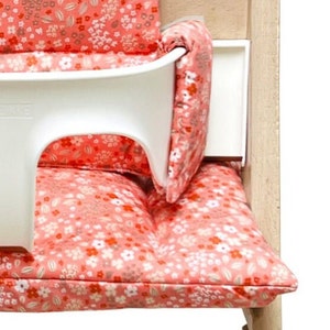 May include: A white high chair with a pink floral patterned cushion. The cushion has a separate back support and a floral pattern.