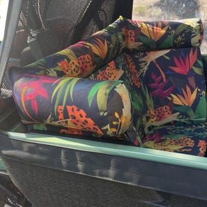 May include: A cargo bike seat with a dark background and a vibrant tropical floral pattern. The seat features a combination of orange, yellow, red, and green leaves and flowers. The seat is designed for comfort and style.