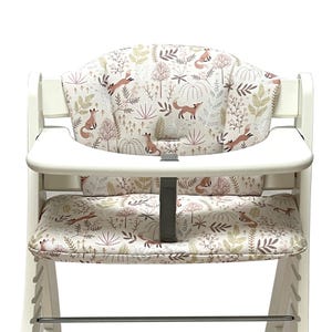 May include: A white high chair with a seat and backrest cushion featuring a woodland fox and foliage pattern in shades of brown, beige, and green. The high chair has a tray and a footrest.