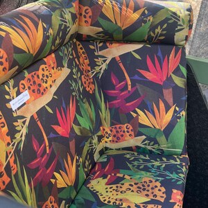 May include: Upholstered outdoor chair cushions with a vibrant tropical print. The cushions feature a dark background with colorful illustrations of leopards, tropical flowers, and foliage in shades of orange, red, green, and yellow.