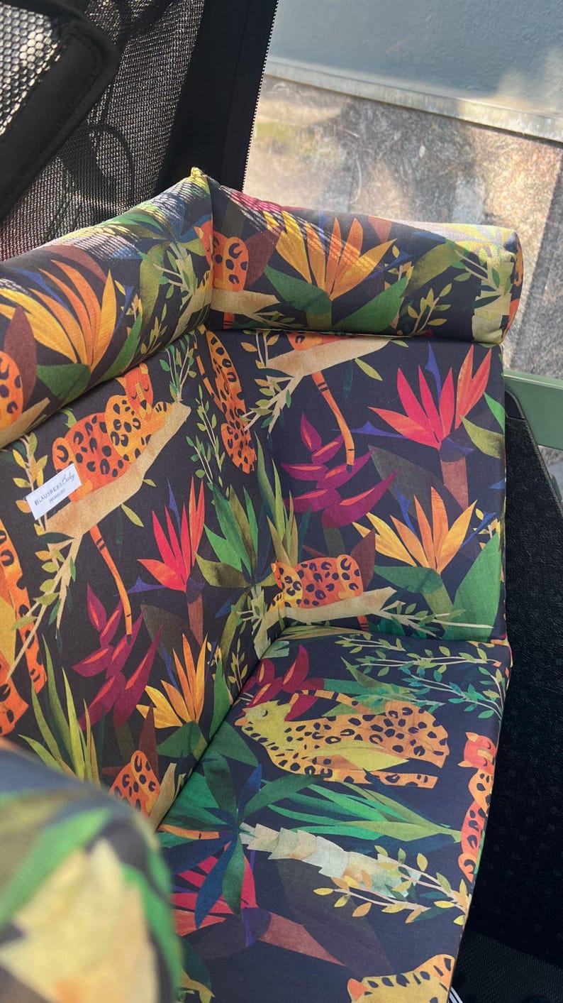 May include: Upholstered outdoor chair cushions with a vibrant tropical print. The cushions feature a dark background with colorful illustrations of leopards, tropical flowers, and foliage in shades of orange, red, green, and yellow.