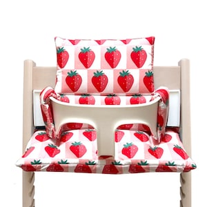 May include: A white high chair with a pink and red strawberry patterned cushion and back support.