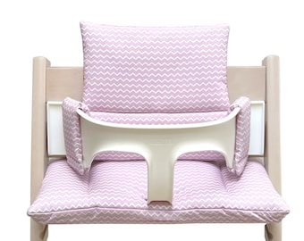 May include: A pink and white chevron patterned high chair cushion with a white tray and armrests.