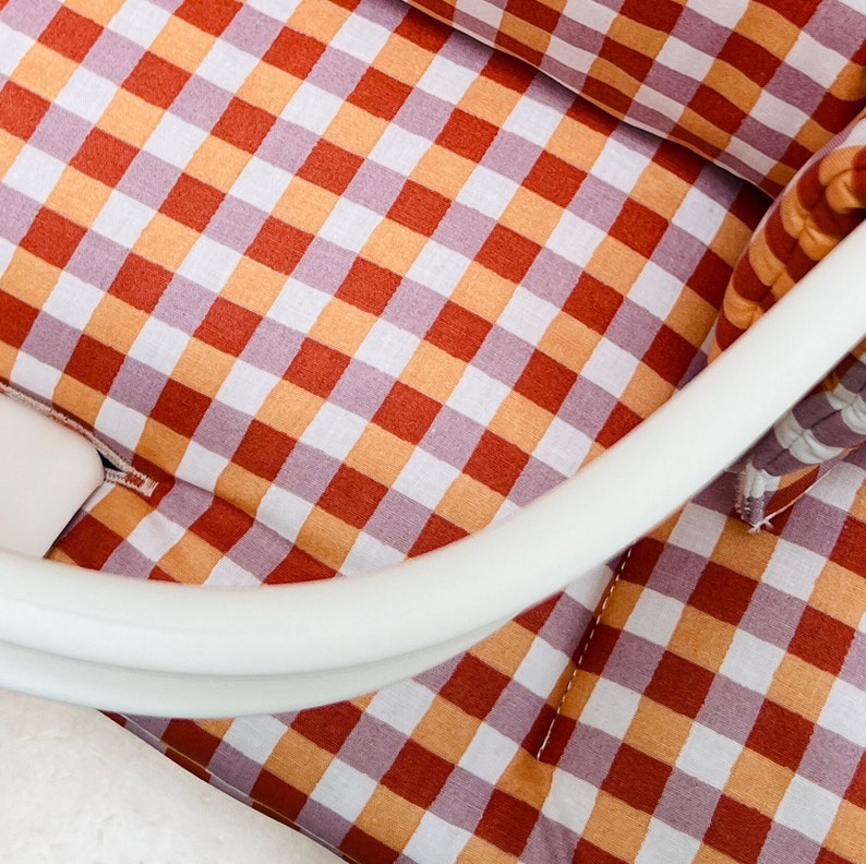 May include: A white crib mattress with a red and orange gingham pattern. The mattress is made of soft, breathable fabric and is perfect for a baby's crib.
