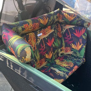 May include: A patterned seat cushion and bolster pillow set featuring a jungle theme with leopards, tropical flowers, and foliage in shades of orange, green, and red against a dark background. The set is designed to fit a cargo bike.