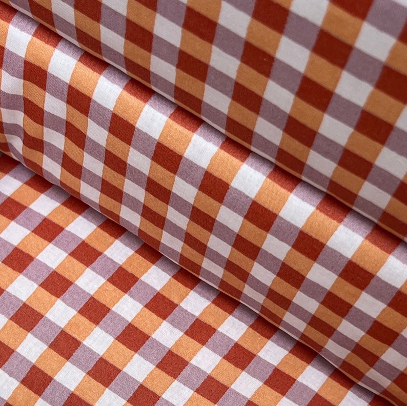 May include: A close-up of a fabric with a red and orange gingham pattern. The fabric is folded in half, creating a diagonal line.