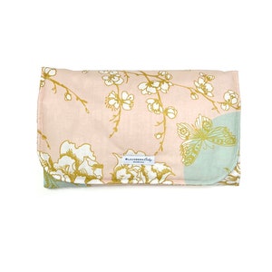 May include: A pink and green changing pad with a gold floral and butterfly design. The pad has a white label that says "Blausberg Baby" in gold lettering.