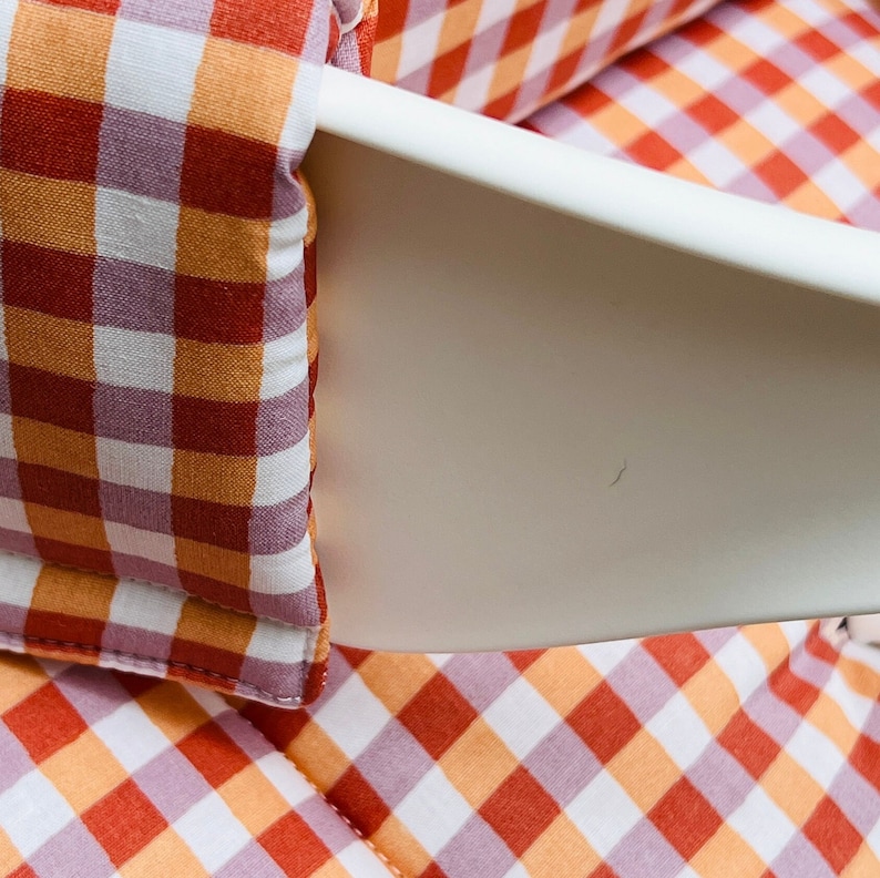 May include: Close-up of a red and orange gingham fabric with white squares. The fabric is folded and has a white seam around the edges.