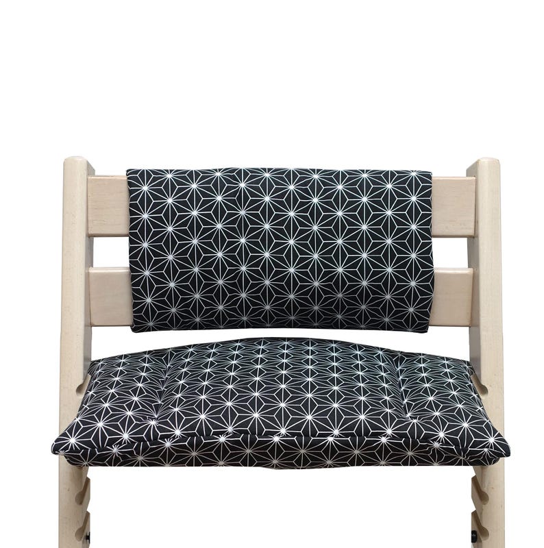 K&ouml;nnte beinhalten: Ein helles Holzhochstuhl mit einem schwarz-wei&szlig;en geometrischen Muster auf Kissen und R&uuml;ckenlehne. Das Muster zeigt wei&szlig;e sternf&ouml;rmige Formen auf schwarzem Hintergrund. Das Design des Stuhls ist modern und minimalistisch.