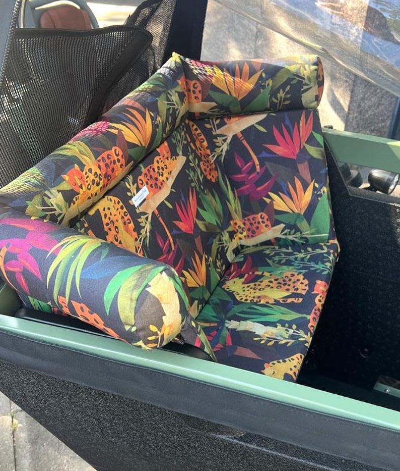 May include: A patterned seat cushion with a tropical design. The cushion features a dark background with colorful illustrations of flowers, leaves, and leopard spots. The cushion is inside a green frame.