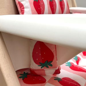 May include: A white high chair with a pink and white gingham pattern cushion and a matching pillow featuring a strawberry print.