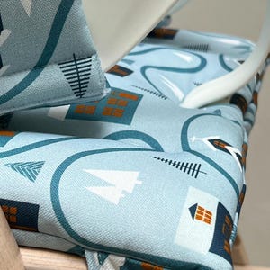 May include: A close-up of a blue and white patterned chair cushion with a geometric design. The cushion is made of fabric and has a brown trim. The cushion is sitting on a wooden chair.