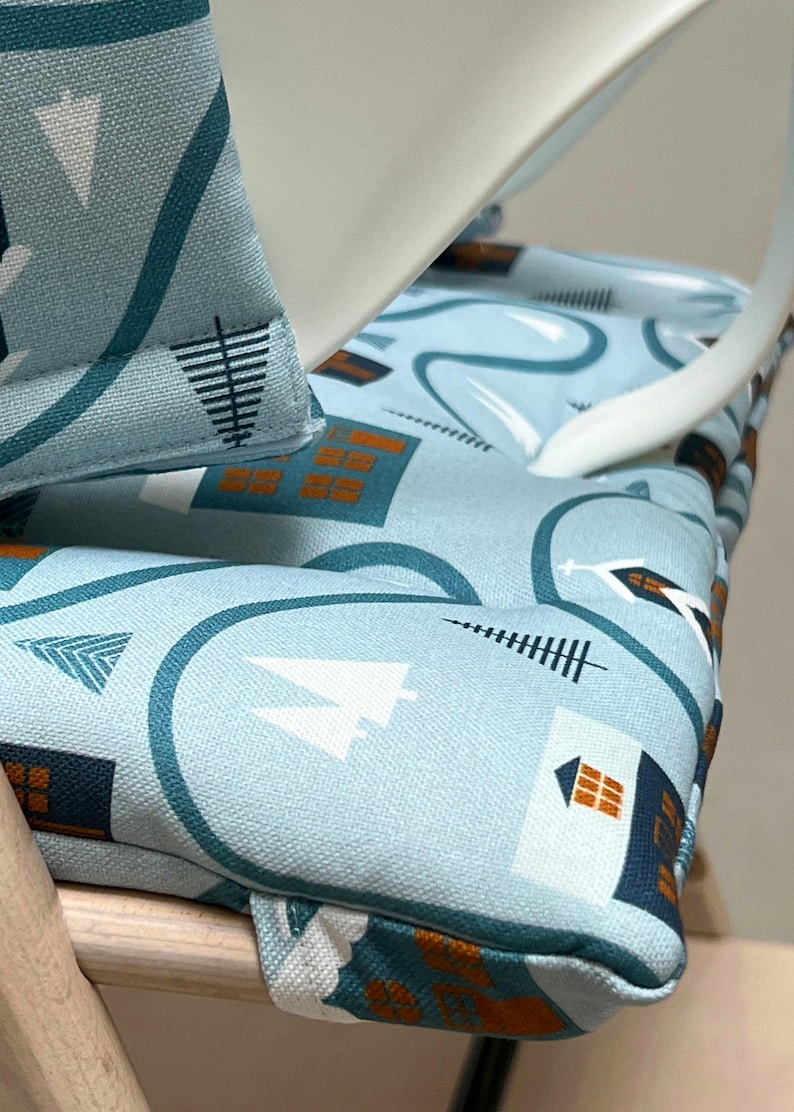 May include: A close-up of a blue and white patterned chair cushion with a geometric design. The cushion is made of fabric and has a brown trim. The cushion is sitting on a wooden chair.