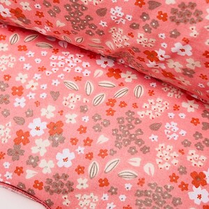 May include: Pink fabric with a floral pattern featuring small white and orange flowers, leaves, and a few hearts. The fabric has a textured surface.