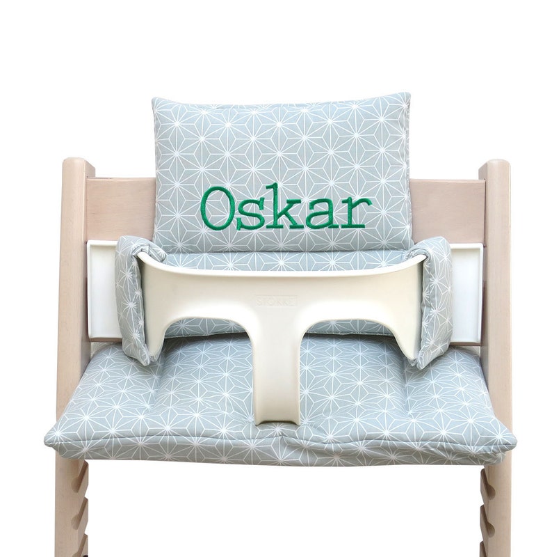 May include: A gray and white geometric patterned cushion with the name "Oskar" embroidered in green on a white high chair.