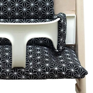May include: A white high chair with a black and white geometric patterned cushion and backrest. The high chair has a white tray and the brand name "STOKKE" is visible on the chair.