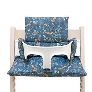 May include: A blue and white patterned high chair cushion with a fox design. The cushion has a white padded back support and a white padded armrest.