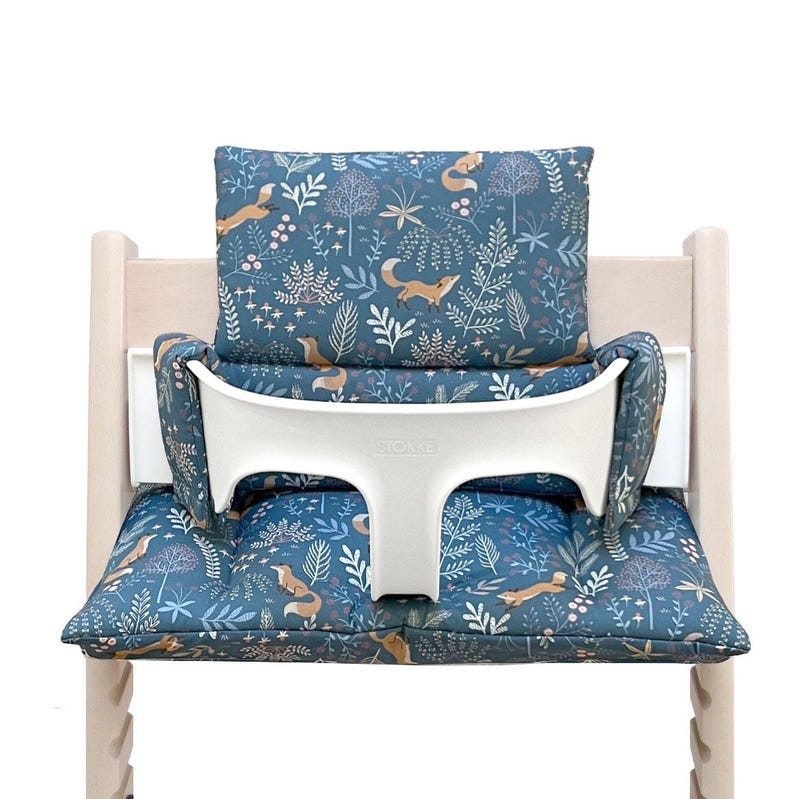 May include: A blue and white patterned high chair cushion with a fox design. The cushion has a white padded back support and a white padded armrest.