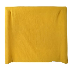 May include: A mustard yellow changing pad made of soft, textured fabric. The pad is folded in half and has a white label on the bottom.