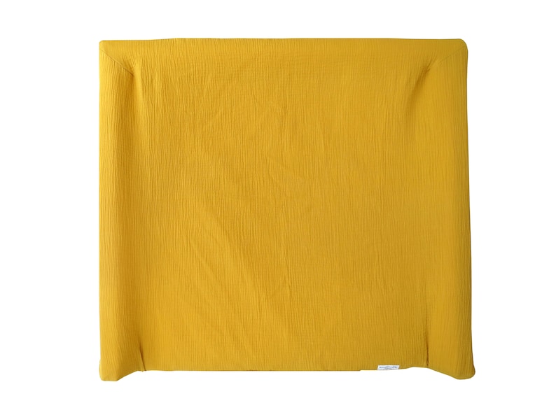 May include: A mustard yellow changing pad made of soft, textured fabric. The pad is folded in half and has a white label on the bottom.