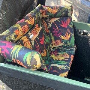 May include: A stroller seat and bolster pillows feature a vibrant jungle print with leopard spots, tropical flowers, and lush green foliage on a dark background. The seat and pillows are inside a green stroller.
