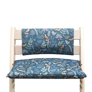 May include: A blue and white patterned high chair cushion with a matching back rest. The pattern features foxes, leaves, and flowers.