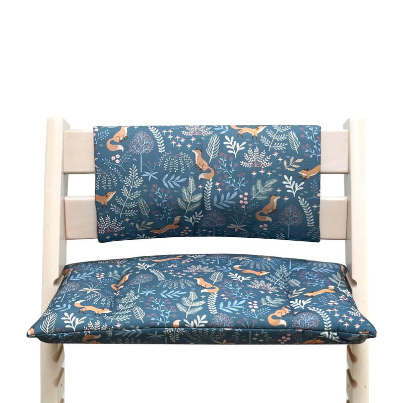May include: A blue and white patterned high chair cushion with a matching back rest. The pattern features foxes, leaves, and flowers.