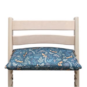 May include: A wooden chair with a blue and orange patterned cushion featuring a woodland design with foxes and leaves. The cushion is padded and provides extra comfort for sitting.