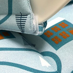 May include: Close-up of a light blue fabric with a white and teal geometric pattern. The fabric has a white seam running along the edge.