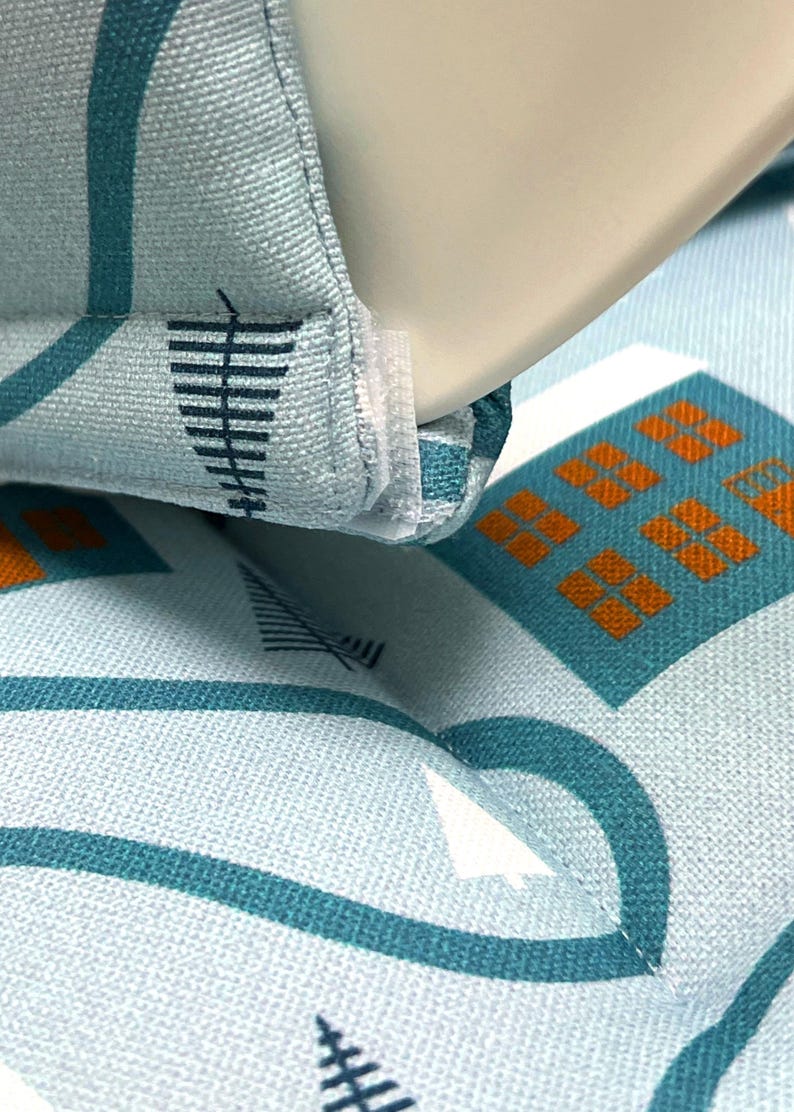 May include: Close-up of a light blue fabric with a white and teal geometric pattern. The fabric has a white seam running along the edge.