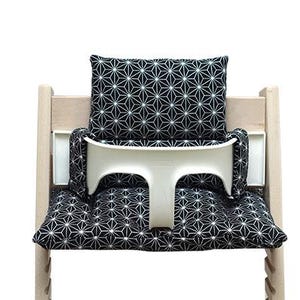 May include: A wooden high chair with a white tray and black and white geometric patterned cushions. The cushions include a seat cushion, back cushion, and side cushions. The high chair is designed for a baby or toddler.