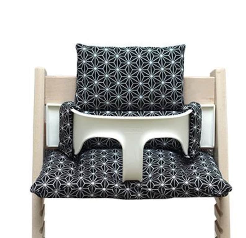 May include: A wooden high chair with a white tray and black and white geometric patterned cushions. The cushions include a seat cushion, back cushion, and side cushions. The high chair is designed for a baby or toddler.