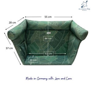 Grünes Babybett mit tropischem Blättermuster. Das Bett ist 55 cm lang, 28 cm breit und 37 cm hoch. Die Innenmaße betragen 51 cm Länge und 44 cm Breite. Der Text "Made in Germany with Love and Care" ist sichtbar.